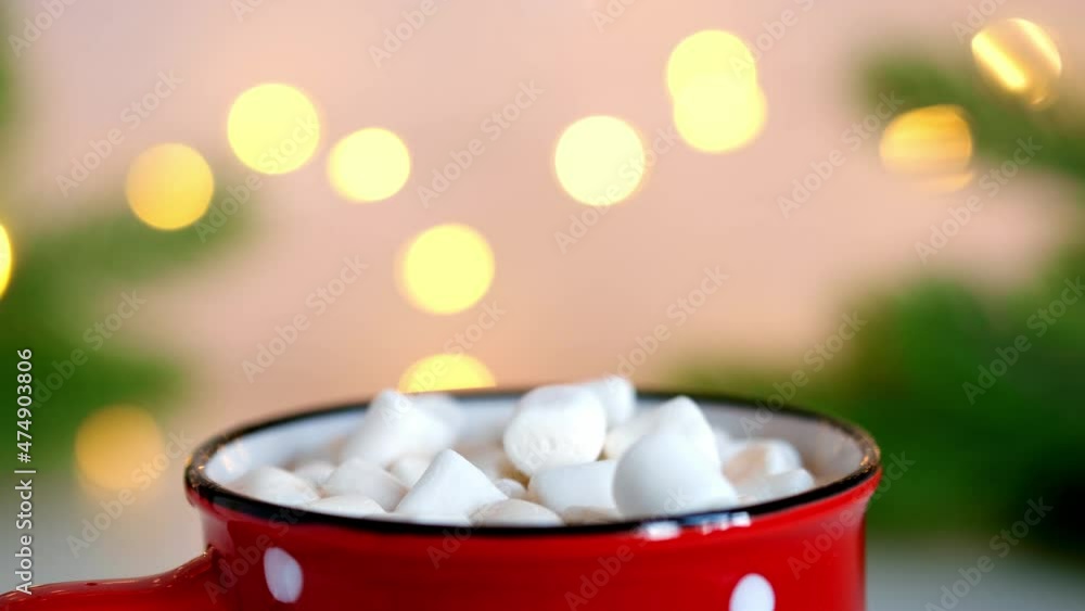 Marshmallows fall into red mug with hot chocolate. Flickering bokeh lights close-up. Slow motion Marshmallows fall into red mug with hot chocolate. Flickering bokeh lights close-up. Slow motion