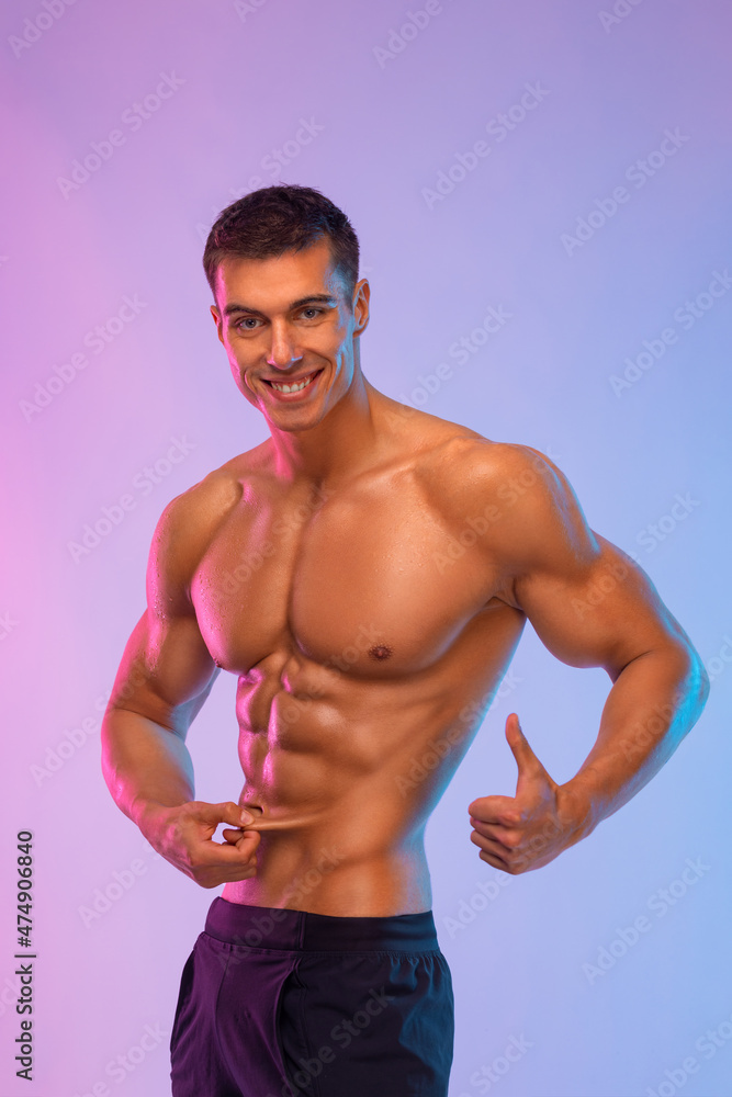 Happy man athlete shows how little subcutaneous fat is in his body. Sportsmen isolated on color background. Fitness motivation. Happy man athlete shows how little subcutaneous fat is in his body. Sportsmen isolated on color background. Fitness motivation.