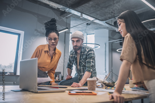 Serious two girls and guy looking into laptop screen