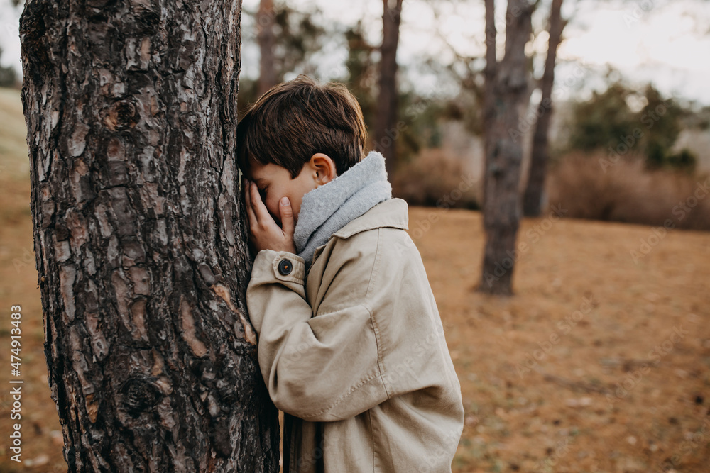 Child playing hide and seek, counting with closed eyes next to a tree in a park. Child playing hide and seek, counting with closed eyes next to a tree in a park.