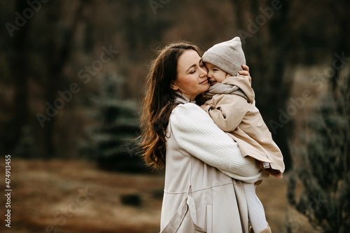 Mother holding little daughter in arms, hugging, outdoors, in a park, on autumn day.