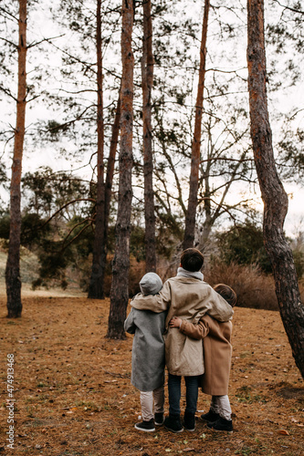 Children hugging, looking up at tall trees in a forest on autumn day.
