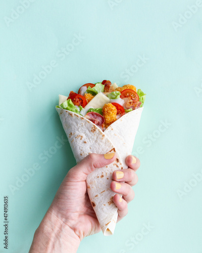 Anonymous person holding chicken wrap with tomatoes and cheese photo