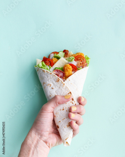 Anonymous person holding chicken wrap with tomatoes and cheese