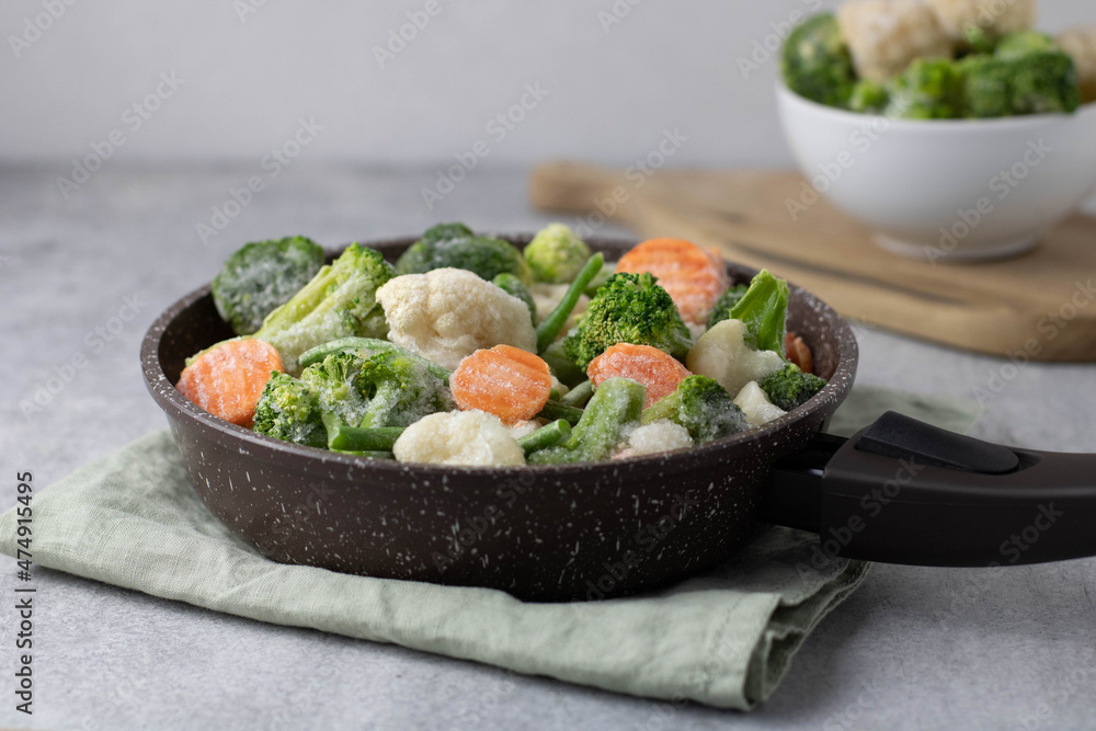 Cooking frozen vegetables: asparagus, broccoli, cauliflower, carrots in pan on a light background, side view