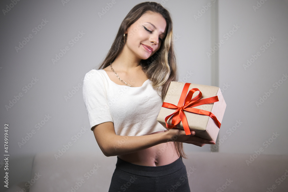smiling woman holding gift box with red ribbon wrapped in kraft paper, indoor photo, smiling woman holding gift box with red ribbon wrapped in kraft paper, indoor photo,