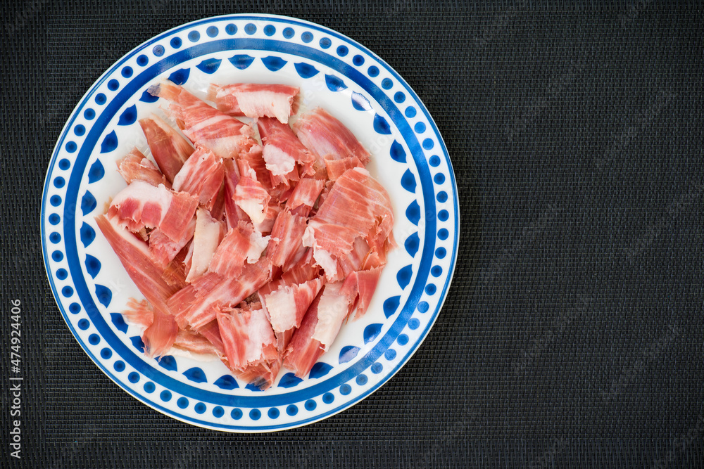 Plato azul, con lonchas de jamón ibérico, sobre fondo negro, vista superior Plato azul, con lonchas de jamón ibérico, sobre fondo negro, vista superior