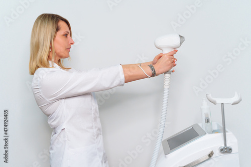 Portrait of master of laser hair removal. Woman in white coat hold laser hair removal device in her hands and show as shoot from it