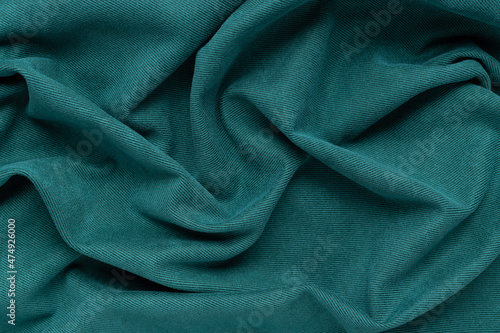 green fabric background with folds. Wavy folds material. Textile and texture concept