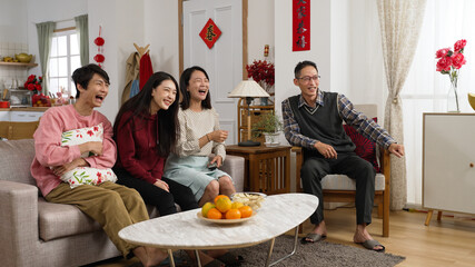 asian family spending spring festival together watching comedy at home. mother using controller and recommending a funny show with gesture. chinese text on door translation: spring and congratulation
