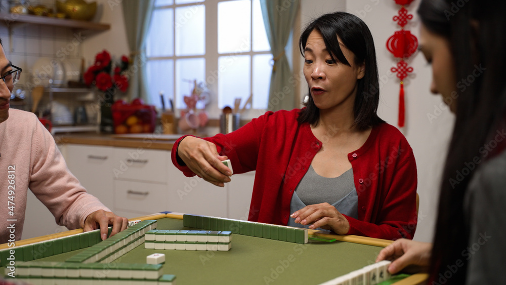 Fototapeta premium selective focus of smiling mother drawing keeping a tile and discarding another from her hand while playing mahjong game at home with family on chinese lunar new year's eve