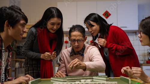slow motion happy father drawing tile in beckoning other mahjong players formoney while his wife and daughter celebrating for his win with clenched fist. word translation  luck