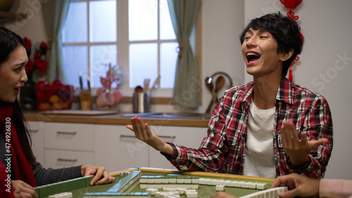 excited son clothing shouting with finger pointing and cheering punching air with fist for winning mahjong game and asking money with beckoning gestures at home during spring festival