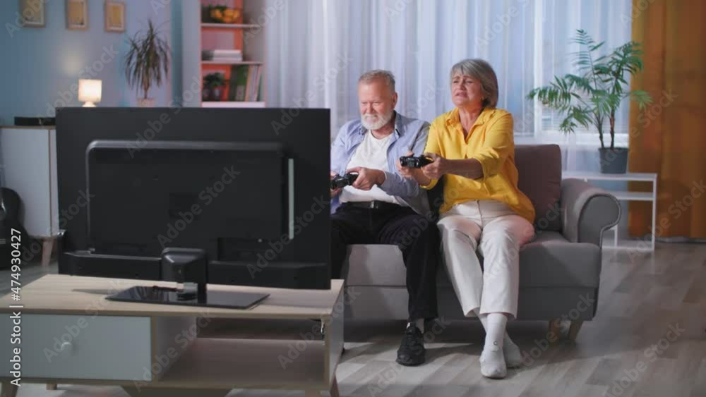 modern male and female retirees have fun playing video games on console while sitting on couch in front of tv during an evening out in living room modern male and female retirees have fun playing video games on console while sitting on couch in front of tv during an evening out in living room