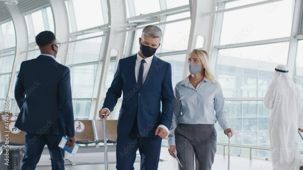 Two business colleagues walk around airport in protective masks with suitcases and talk while discussing business trip. Two business colleagues walk around airport in protective masks with suitcases and talk while discussing business trip.
