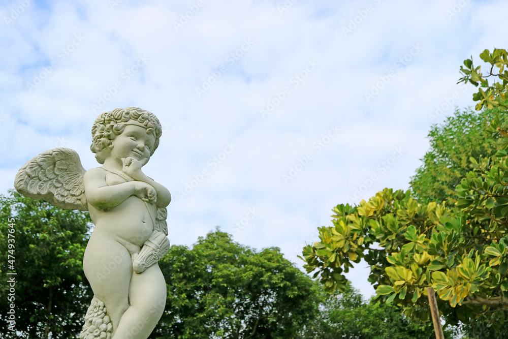 Closeup an adorable cupid sculpture in the garden against fluffy cloudy sky Closeup an adorable cupid sculpture in the garden against fluffy cloudy sky