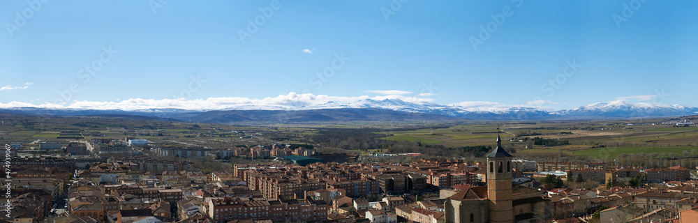Panoramic view of South West part of the city in Avila, Spain. The St. Nicholas Church in the foreground and the Sierra de Gredos mountain range covered with snow in the background.