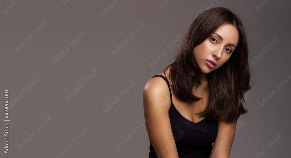 Fototapeta premium Hair or skin care concept. Portrait of a luxurious young woman with healthy hair and skin on studio gray background free space for text