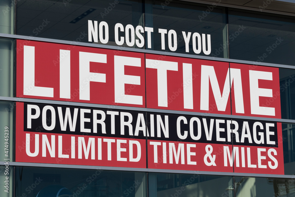 NO COST TO YOU LIFETIME POWERTRAIN COVERAGE UNLIMITED TIME AND MILE sign at a car dealership.