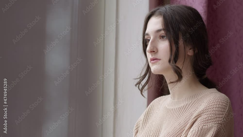 A sad girl stands at the window thoughtfully looking into the distance. A sad girl stands at the window thoughtfully looking into the distance.