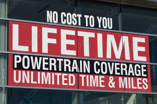 NO COST TO YOU LIFETIME POWERTRAIN COVERAGE UNLIMITED TIME AND MILE sign at a car dealership.