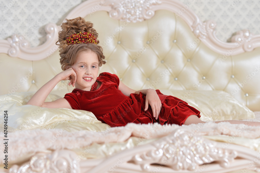 Fototapeta premium cute little girl in red dress lying on bed