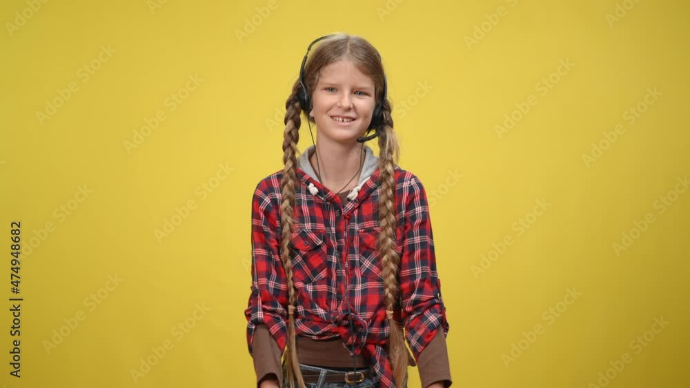 Positive Caucasian teenage girl in headphones with microphone talking gesturing at yellow background. Portrait of beautiful slim teenager explaining issues looking around. Confidence and speech Positive Caucasian teenage girl in headphones with microphone talking gesturing at yellow background. Portrait of beautiful slim teenager explaining issues looking around. Confidence and speech