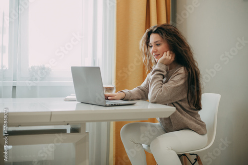 Smiling young 30 years old brunette woman with long hair using laptop at home
