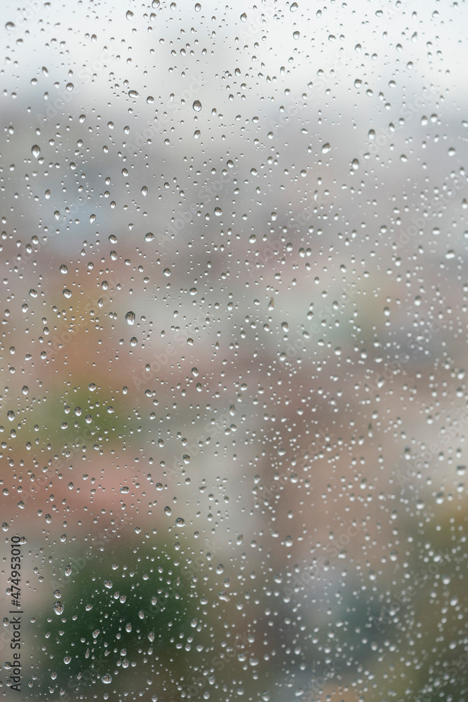 rain drops on windowpane over blurred city view with buildings or houses