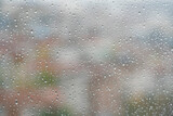rain drops on windowpane over blurred city view with buildings or houses