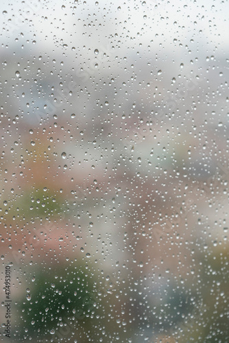 rain drops on windowpane over blurred city view with buildings or houses