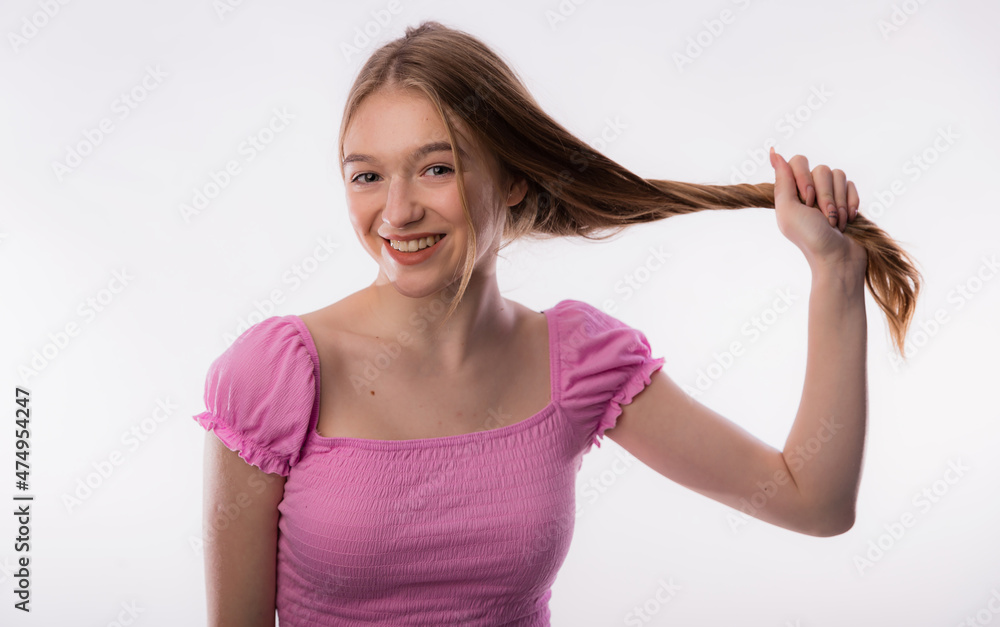Cute young woman pulling her long blond hair. Beautiful female holding hair up on white background copy space. Care and health concept of the head and hair Cute young woman pulling her long blond hair. Beautiful female holding hair up on white background copy space. Care and health concept of the head and hair