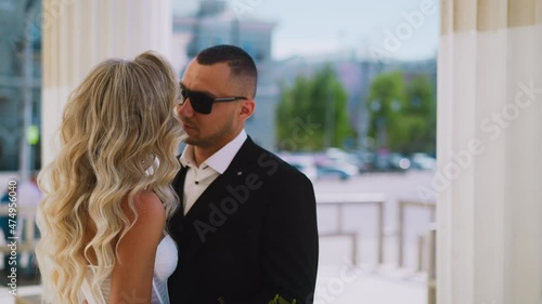 Man with sunglasses hugs beloved wife with hairdo by columns photo