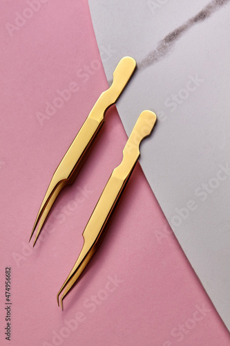 Golden Tools for Eyelash Extension Procedure. Two golden tweezers on marble plate.On pink background.Beauty and fashion concept