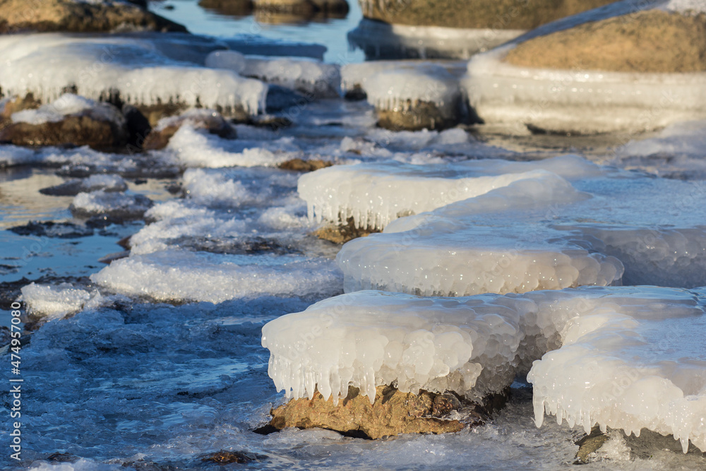 Winter landscape with ice and stones on frozen Sea. Ice frozen on a stone. Sea shore in winter, covered with ice and snow Winter landscape with ice and stones on frozen Sea. Ice frozen on a stone. Sea shore in winter, covered with ice and snow