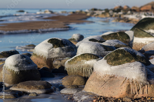 Winter landscape with ice and stones on frozen Sea. Ice frozen on a stone. Sea shore in winter, covered with ice and snow