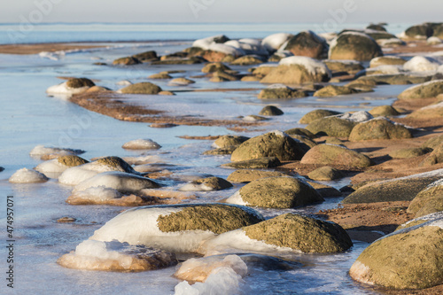 Winter landscape with ice and stones on frozen Sea. Ice frozen on a stone. Sea shore in winter, covered with ice and snow