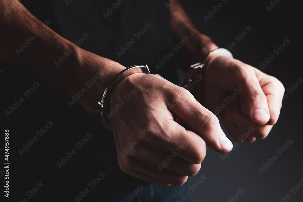 a young man in a shirt stands in handcuffs