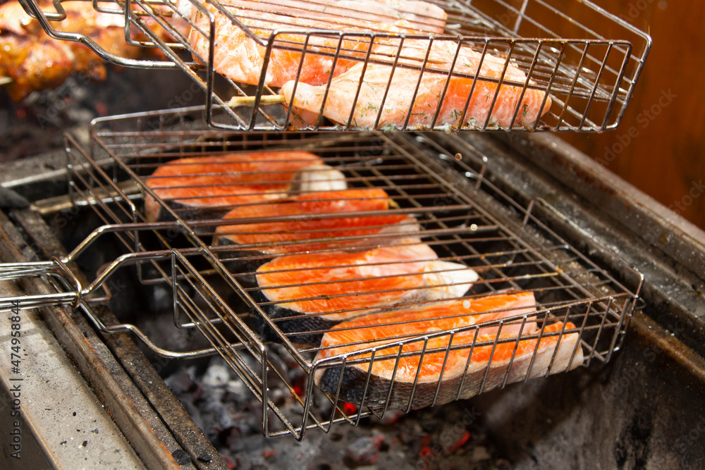Grilled fish steaks on fire. Charcoal cooking of salmon steaks, pieces of fish on wooden grill above the coals. hand with spatula straightens food, outdoors.