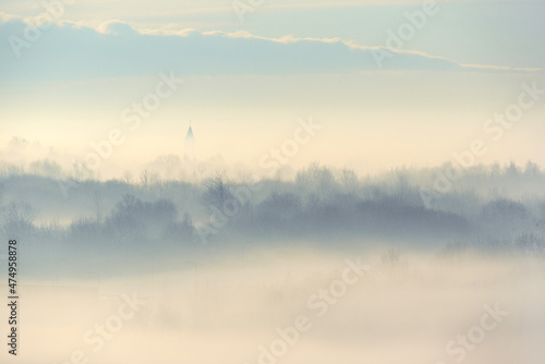 Outlines of trees and church in the fog creeping. Winter landscape