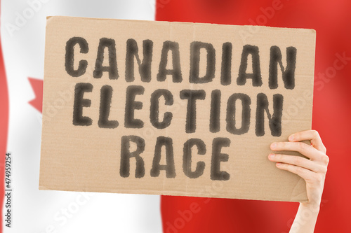 The phrase " Canadian election race " on a banner in men's hand with blurred Canadian flag on the background. Ballot box. Politics. Conflict. Politic. Primary. Selection. Choosing. Ottawa