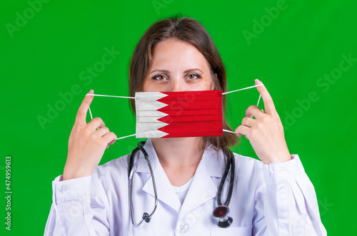 Woman doctor in a medical coat holds a medical mask with of the Bahrain flag