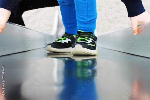Partial view of a child on a playground slide, reflection in metal surface.