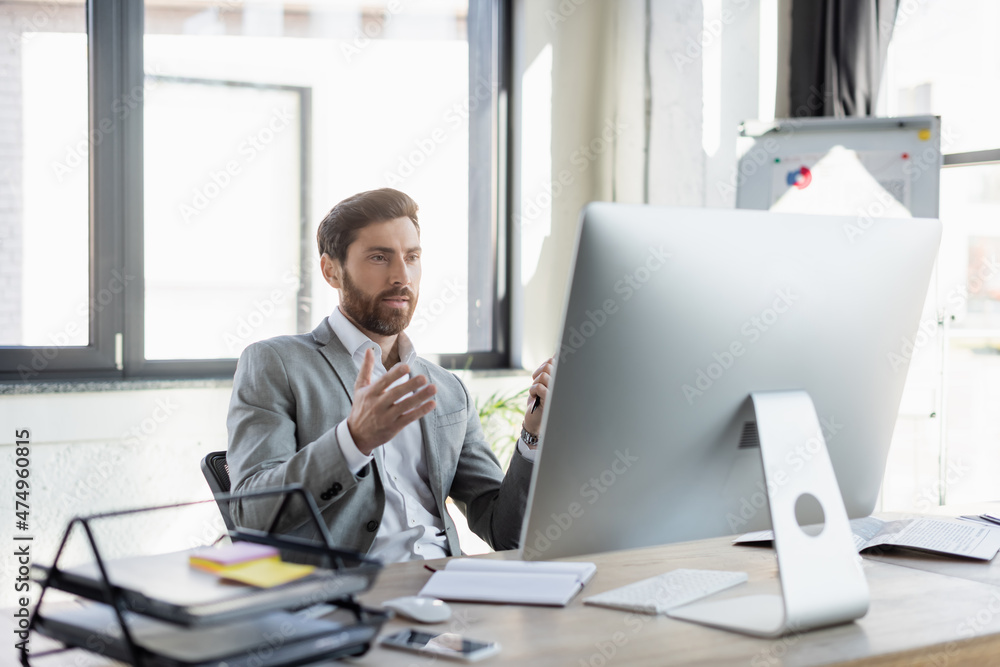 Bearded businessman having video call on computer near newspaper and notebook in office. Bearded businessman having video call on computer near newspaper and notebook in office.