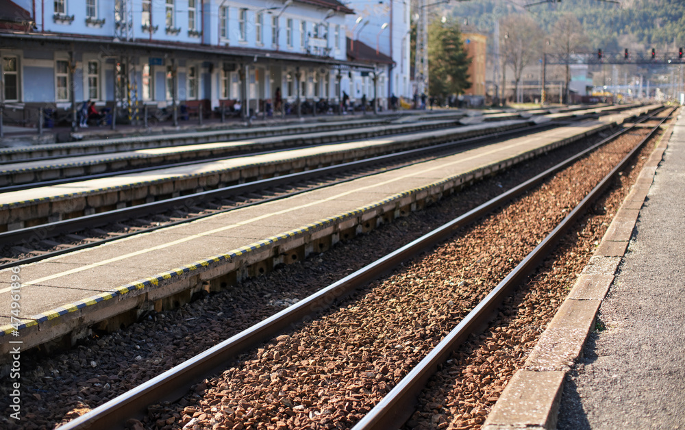 Train station in small city on sunny day, shallow depth of field photo, focus on concrete platform and steel rail foreground