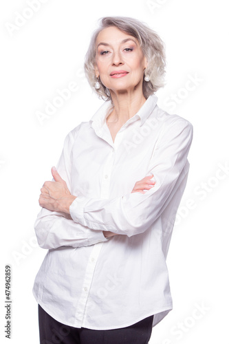Happy trendy senior woman with a beautiful smile wearing a fashionable shirt standing with her arms crossed looking at the camera isolated on white background