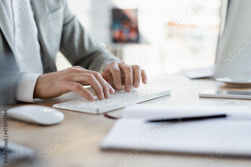 Cropped view of businessman typing on keyboard near smartphone and blurred notebook in office.