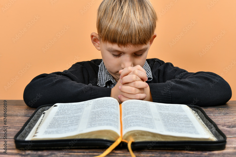 An open Bible in front of a praying child with folded hands.