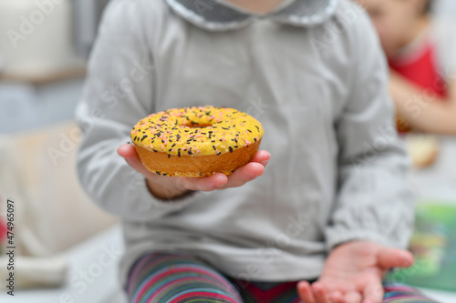 A little girl sits at the table in the kitchen and holds a sweet donut with frosting in her hand.