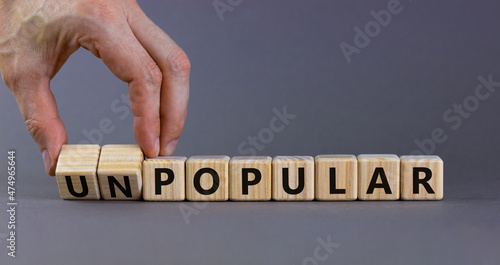 Popular or unpopular symbol. Businessman turns wooden cubes and changes the word unpopular to popular. Beautiful grey table, grey background. Popular or unpopular and business concept. Copy space. photo